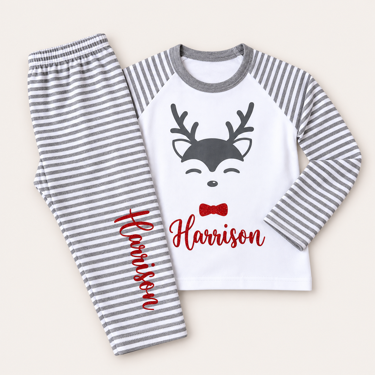 Personalised grey stripe Christmas reindeer pyjamas laid flat with a festive reindeer design and red bow, Grace & Grayson