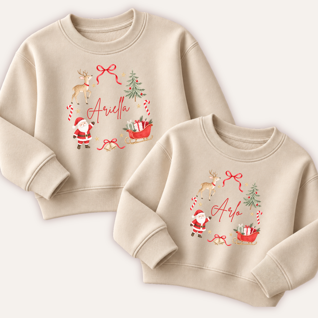 Two personalised cream Christmas sweatshirts featuring Santa, a reindeer, Christmas tree and gift-filled sleigh arranged in a wreath around a name. Grace & Grayson.