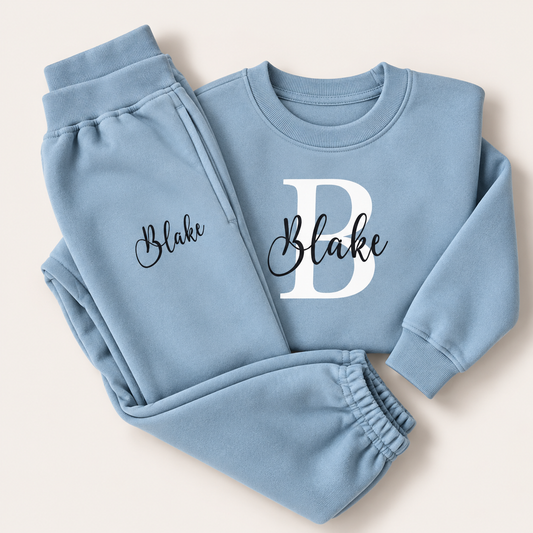 Dusty blue personalised sweatshirt and joggers with a white initial and black script name, laid flat, Grace & Grayson