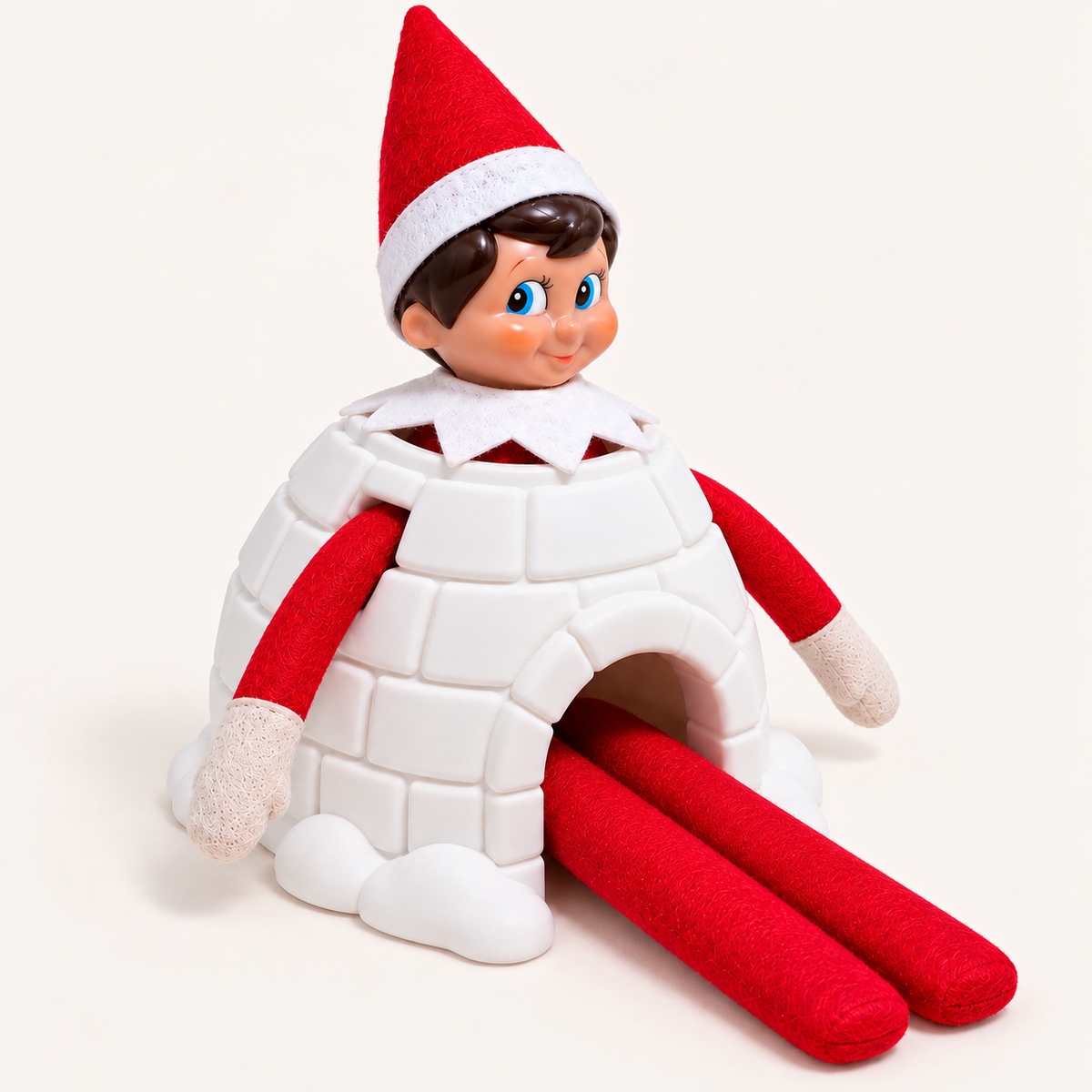 Angled view of a Christmas elf on the shelf wearing a white 3D-printed igloo costume with a red hat and limbs, against a light background, Grace & Grayson.