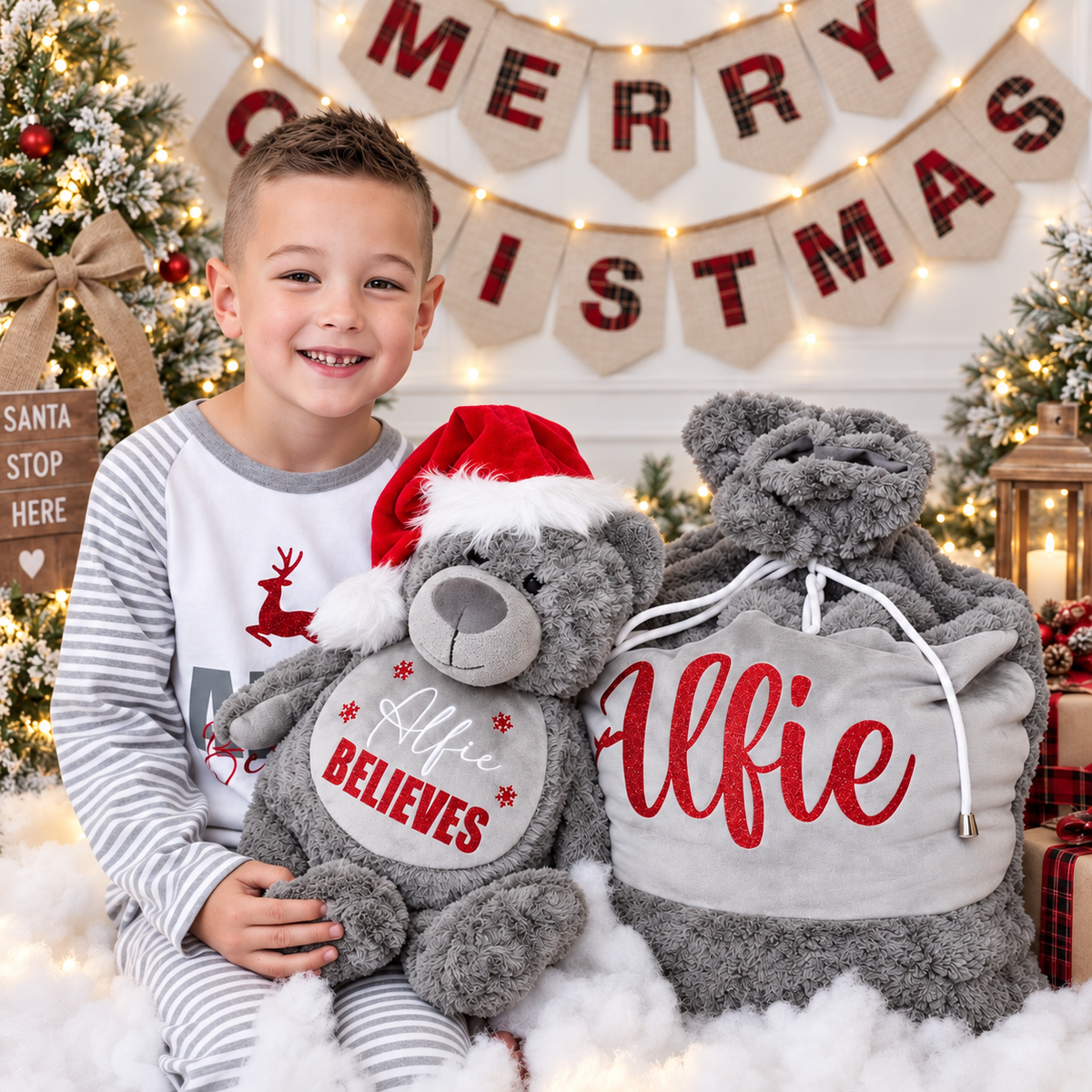 Child holding a grey personalised Believes Christmas teddy wearing a Santa hat beside a matching Christmas sack in a festive setting, Grace & Grayson
