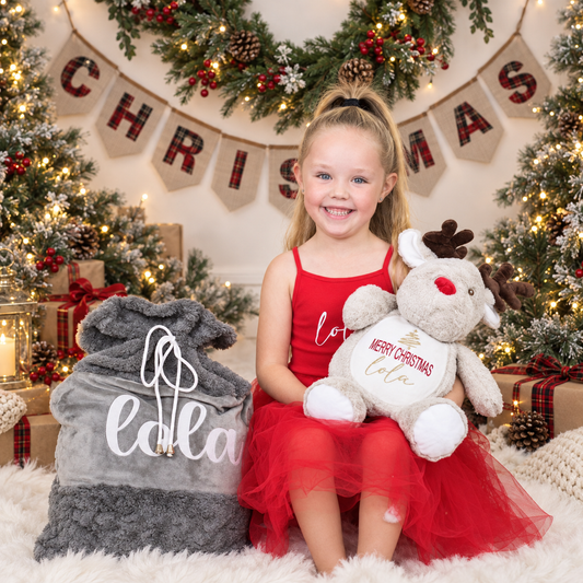 Child holding a light brown reindeer Christmas teddy wearing beside a grey personalised Christmas sack in a festive setting, Grace & Grayson