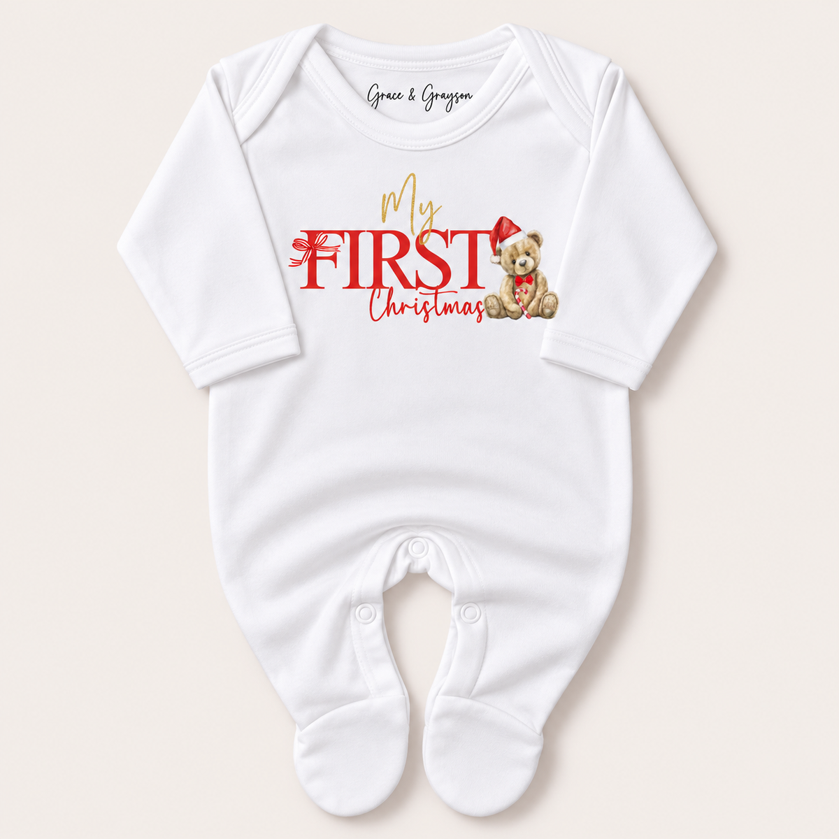 White footed baby grow with red and gold “My First Christmas” lettering and a teddy bear in a Santa hat, Grace & Grayson.