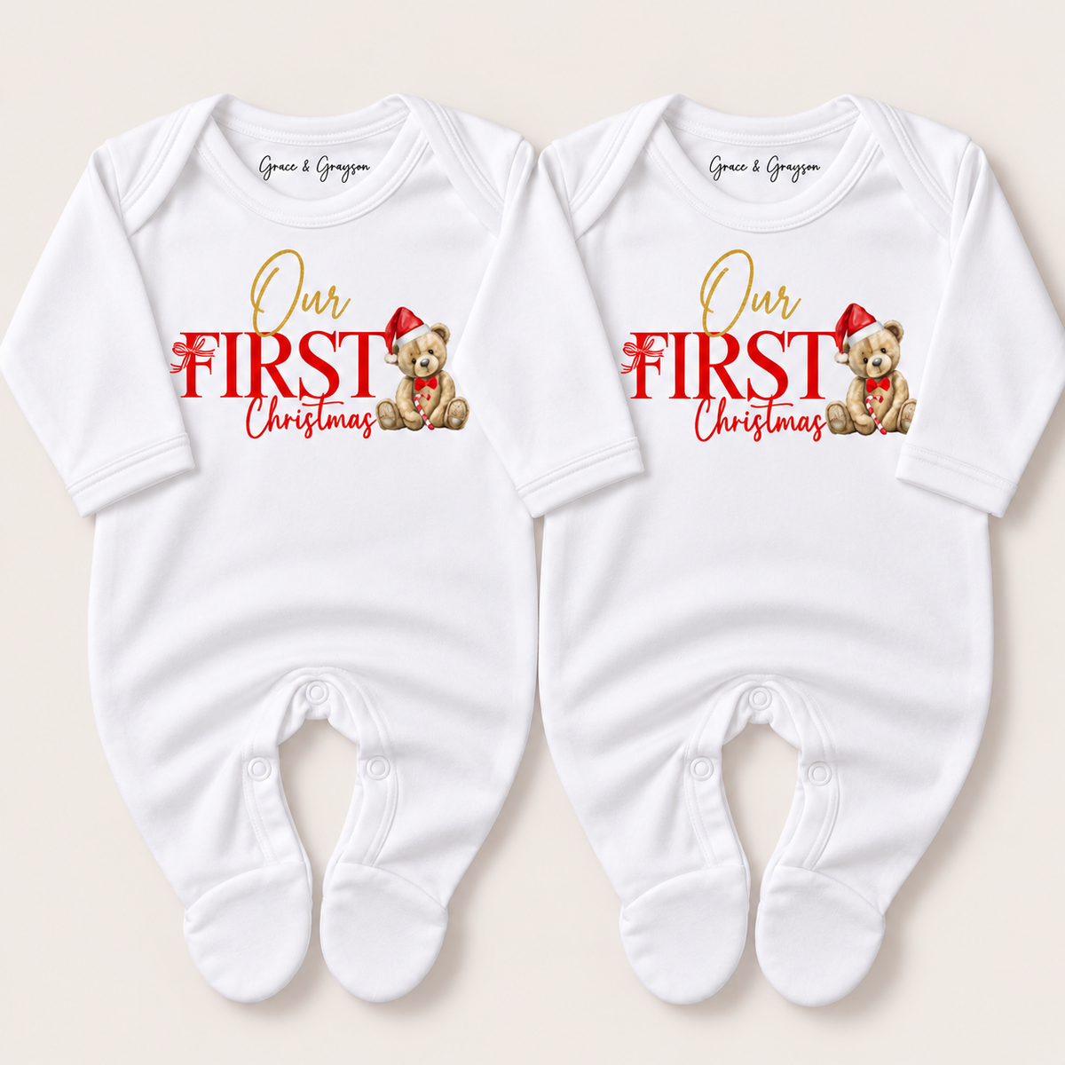 Pair of white footed baby grows with red and gold “Our First Christmas” lettering and teddy bears in Santa hats, Grace & Grayson.