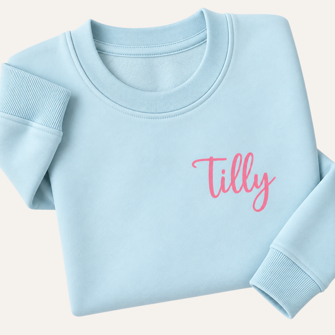 Pastel blue personalised sweatshirt with a small pink script name on the chest, folded on a light background | Grace & Grayson