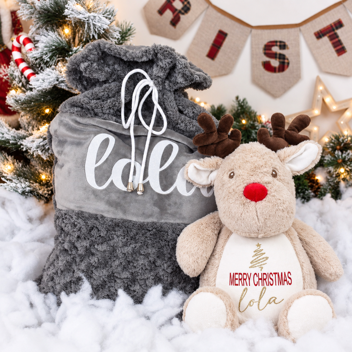 Light brown reindeer Christmas teddy beside a grey personalised Christmas sack with a festive Christmas tree background, Grace & Grayson