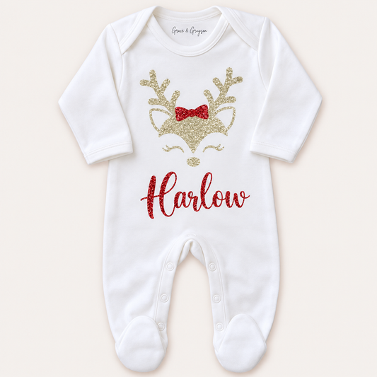 White footed Christmas baby grow photographed front-on, with a gold reindeer face, red bow and red glitter name detail, Grace & Grayson.