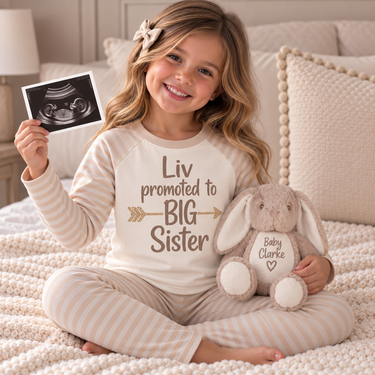 Child wearing cream striped personalised pyjamas with “Promoted to Big Sister” lettering, holding an ultrasound photo, Grace & Grayson.
