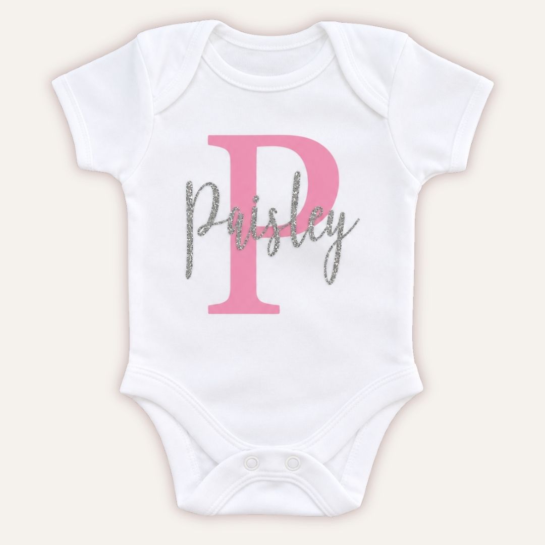 White personalised baby vest with a large pink initial and silver glitter script name, displayed on a light background, Grace & Grayso