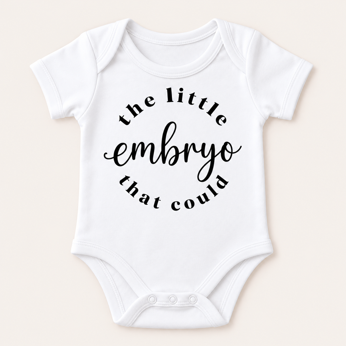White short-sleeved baby vest with “the little embryo that could” printed in black, laid flat on a cream background. Grace & Grayson.